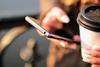 Close-up of a person holding a smartphone and a disposable coffee mug