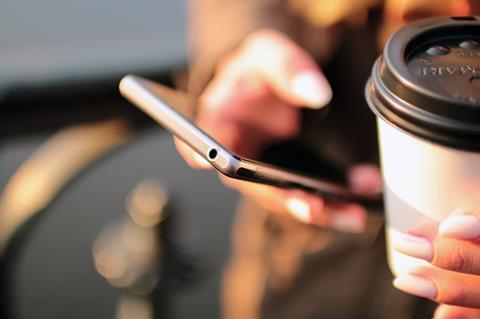 Close-up of a person holding a smartphone and a disposable coffee mug